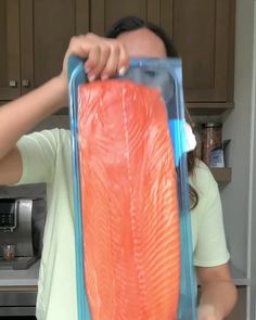 a woman holding up a large piece of salmon in a plastic bag over her face