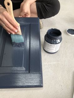 a woman is using a brush to paint a cabinet door with dark blue varnishing