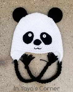 a crocheted panda bear hat with black ears on it's head, sitting on the ground