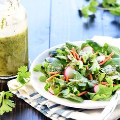 a white plate topped with a salad next to a jar of dressing