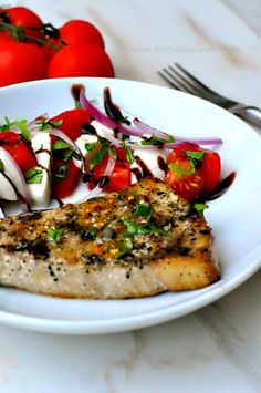 a white plate topped with fish next to red onions and cherry tomatoes on top of a table