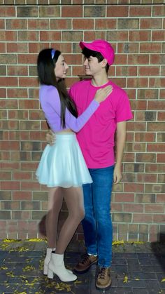 two people standing next to each other near a brick wall