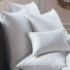 white pillows piled on top of each other in front of a wall with a clock