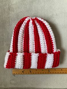 a red and white knitted hat sitting on top of a measuring tape next to a ruler