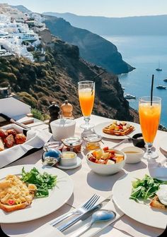 an outdoor table with food and drinks overlooking the water's edge on a sunny day