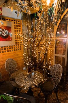 a table and chairs in a room with lights on the wall above it, along with a tree that has been decorated for christmas