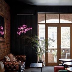 a living room filled with lots of furniture next to a brick wall covered in neon signs