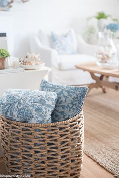 a wicker basket with blue and white pillows on the floor in a living room