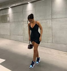 a woman in a black dress is holding a handbag