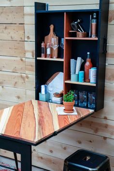 a wooden table sitting in front of a shelf filled with bottles and other items next to a stool