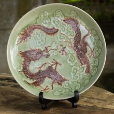 a green and brown plate with two dragon designs on the front sitting on a wooden table