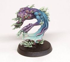 a figurine of a blue and purple creature on a black base with green leaves