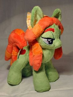 a green and orange pony stuffed animal sitting on top of a white sheeted surface