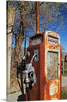 an old rusty gas pump sitting on the side of a road next to a tree