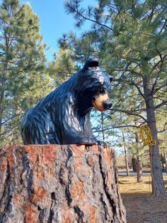 a statue of a bear sitting on top of a tree stump in front of some trees