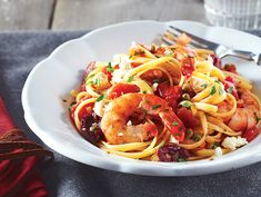 a white bowl filled with pasta and shrimp on top of a blue napkin next to a fork