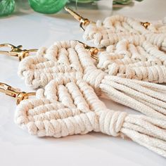 two pairs of white rope earrings with gold hardware on top of a table next to green leaves