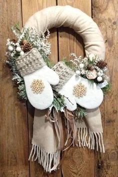 a wreath with white mitts and greenery on it hanging from a wooden door