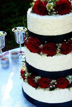 a three tiered wedding cake with red roses on the top and bottom, sitting on a table