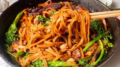 someone is holding chopsticks over some noodles and broccoli in a skillet