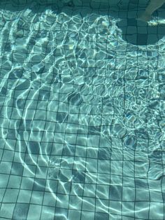 a person swimming in a pool with clear blue water and tiles on the floor,