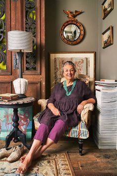 an older woman sitting on a chair in front of a stack of papers and a lamp