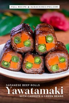 japanese beef rolls with carrots and green beans on a white plate next to flowers