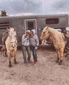 two people standing next to horses in front of a trailer