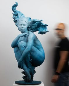 a man standing next to a blue sculpture in front of a white wall with a woman on it