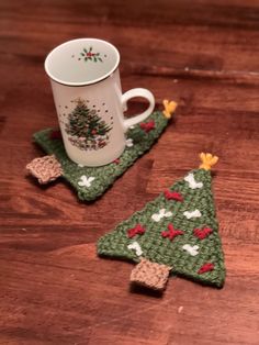 two crocheted christmas tree coasters and a coffee cup on a wooden table