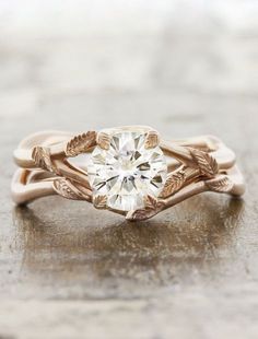 an engagement ring with leaves on the band and a round diamond in the center, sitting on top of a table