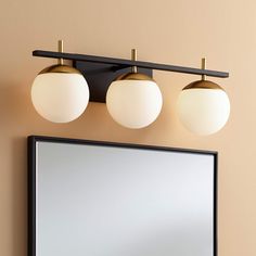 a bathroom mirror with three lights above it and a light fixture on the wall next to it