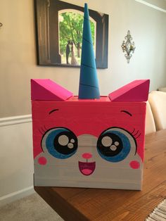 a pink box with a cat's face painted on the side and a blue hat on top