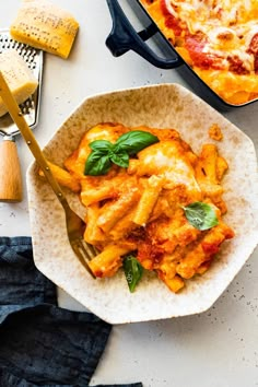 a pasta dish with basil and cheese in a white bowl next to a spatula