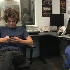 two men sitting in an office looking at their cell phones, one on the phone