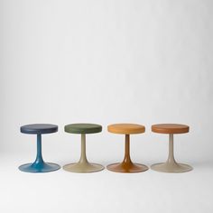 three different colored stools sitting next to each other on a white surface in front of a wall