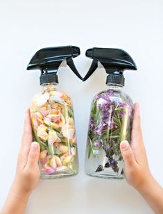 two hands holding jars filled with flowers on top of a white table next to each other