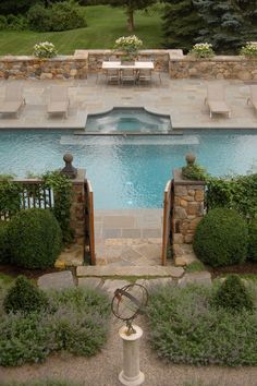 an aerial view of a swimming pool surrounded by greenery and stone fenced in area