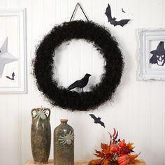 a black wreath with bats hanging on the wall next to two vases and an owl