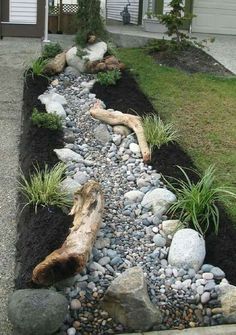 a garden with rocks, grass and plants in the ground next to a wooden log