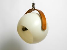 an apple hanging from a hook on a white wall with a brown leather strap around it