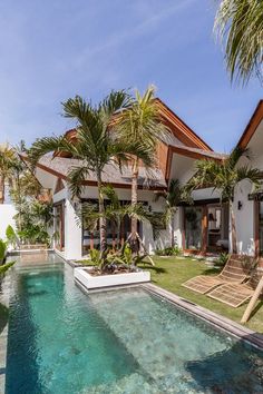 a pool in front of a house with palm trees and lawn chairs on the side