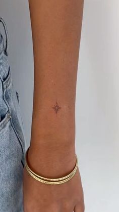 a woman's arm with a tiny star tattoo on it and a gold bracelet