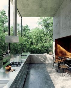 an outdoor kitchen with table and chairs next to the counter top, overlooking trees in the background