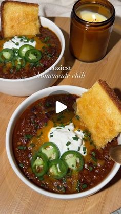 two bowls filled with chili, cheese and bread on top of a wooden cutting board