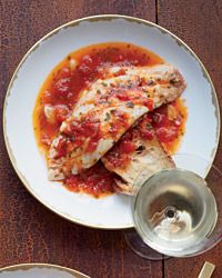 a white plate topped with fish covered in sauce next to a glass of wine on top of a wooden table