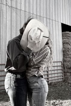 black and white photograph of two women hugging in front of a barn with hay bales