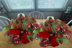 two red and green christmas wreaths sitting on top of a wooden table next to a window