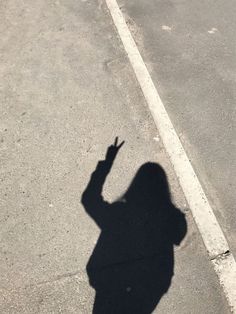 the shadow of a person holding a cell phone in one hand and pointing at something on the other