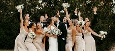 a group of people standing next to each other holding bouquets in the air with their hands up